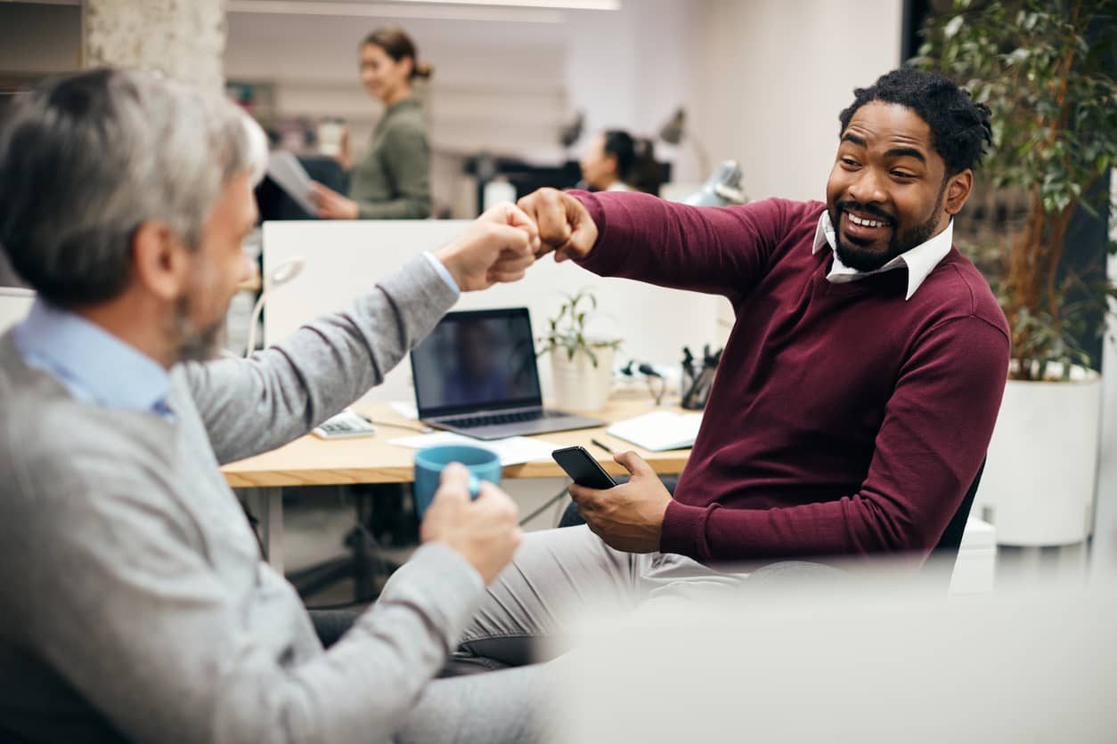 Two male coworkers at desks engage in a fist bump